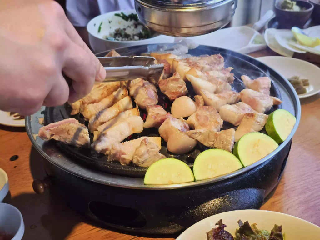 직원이 집게를 들고 알맞게 달궈진 불판 위에 두툼한 숙성육과 곁들임 애호박을 올려 굽기 시작